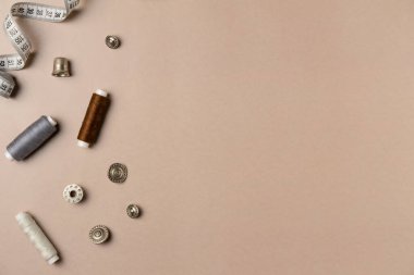 Bej arka planda aksesuarlar dikiyorum. Ölçüm bandı, iplik, düğmeler, yüksük, bobbin. Düz yerde, üst tarafta. Boşluğu kopyala