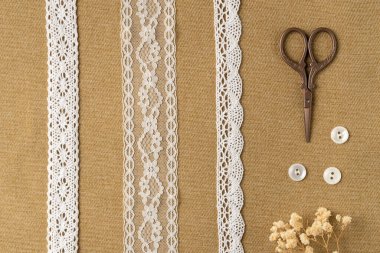 Kumaş zemin üzerinde farklı klasik kurdeleler, düğmeler ve makas. Düz yatış, üst görünüm.