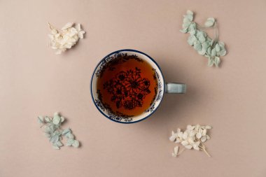 Yukarıdan bej arka planda çiçekli bir fincan çay. Düz yatış, üst görünüm.