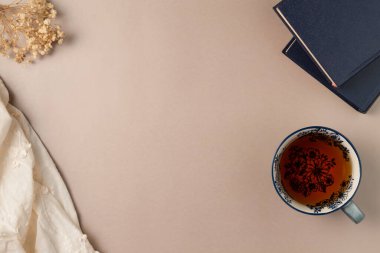 Yukarıdan gelen bej arkaplanlı çay ve çiçekli kitaplar. Düz yerde, üst tarafta. Boşluğu kopyala