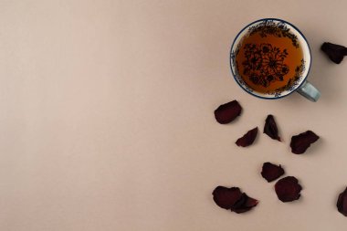 Yukarıdan bej arkaplanlı gül yapraklı bir fincan çay. Düz yerde, üst tarafta. Boşluğu kopyala