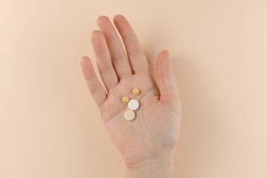 Bej arka planda bir kadının elindeki haplar. Düz yatış, üst görünüm.