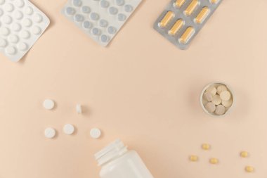 Bej arka planda farklı haplarla dolu bir sürü kabarcık ve şişe. Düz yatış, üst görünüm.