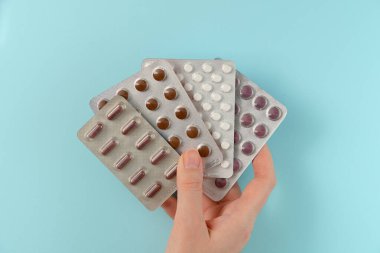 Mavi arka planda, bir kadının elinde farklı haplar bulunan bir sürü kabarcık. Düz yatış, üst görünüm.