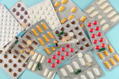 Mavi arka planda farklı haplar ve şırıngalarla su toplamış. Düz yatış, üst görünüm.