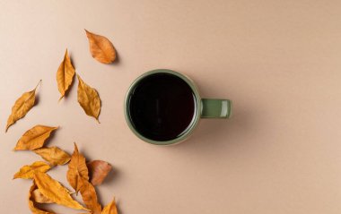 Bej arka planda yaprakları olan bir fincan çay. Düz yatış, üst görünüm.