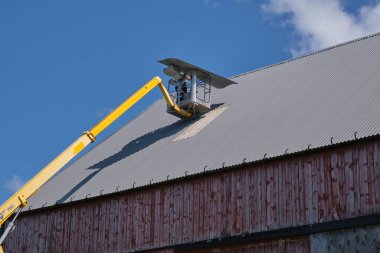 Skaraborg İsveç 'te güneşli bir yaz gününde sarı bir manlift ile bir tarım binasının düz çatısını onarmak.