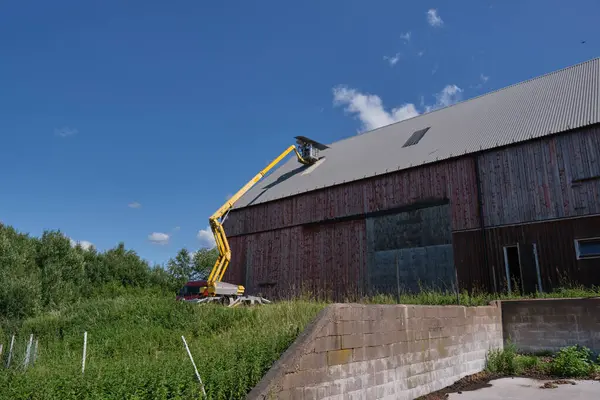 Stock image Repairing a flat roof of an agricultural building with a yellow manlift on a sunny summer day in Skaraborg Sweden