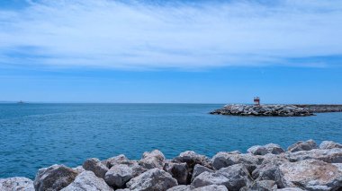 Rocky Shoreline ve Blue Sky Horizon Altında Uzak Deniz feneri Manzarası