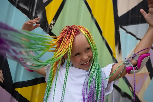 stock image portrait of a little beautiful girl with multi-colored pigtails on the background of a colorful wall.