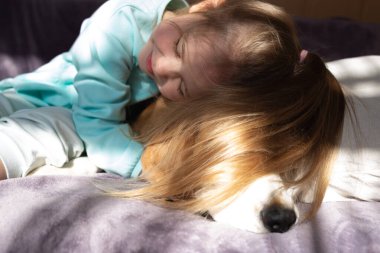 Küçük tatlı kız pencere kenarında oturan av köpeğine sarılıyor..