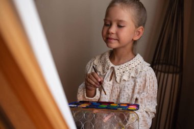 Küçük tatlı kız resim çiziyor, resim sehpasında tuvale boyalar çiziyor..