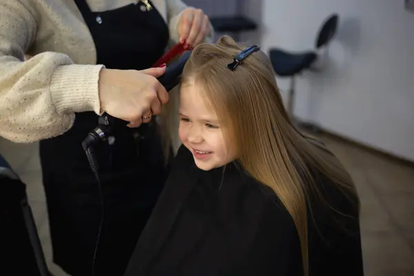 the hairdresser in the barbershop combing the hair of a little cute girl.
