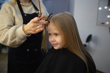 Berber dükkanındaki kuaför küçük tatlı bir kızın saçını tarıyor..