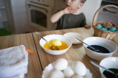 Küçük şirin çocuk paskalya için yumurta boyuyor. Mutfakta, masada oturuyor..
