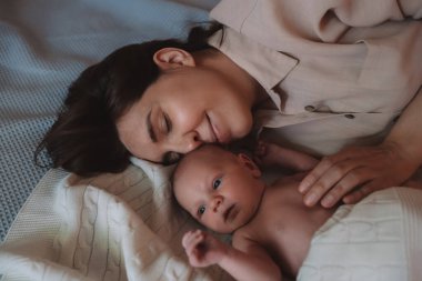 Genç ve güzel anne, yeni doğmuş bebeğini yatak odasında yatarken öper..