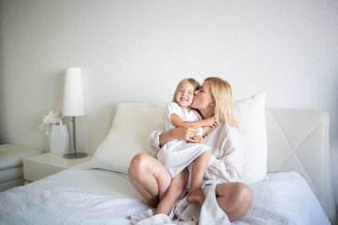 Küçük kız yatak odasında yatakta otururken annesine sarılıyor..