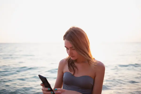 portrait of a young beautiful woman typing a text message on the phone on the seashore.