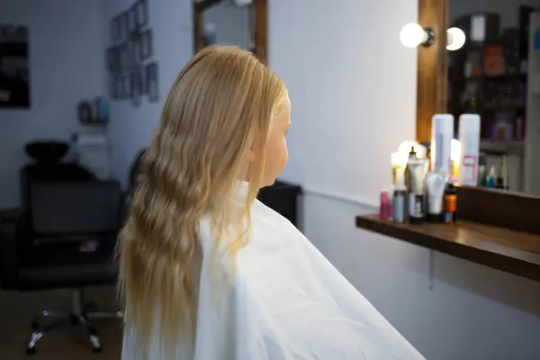 hairdresser straightens hair of a little girl in a beauty salon.