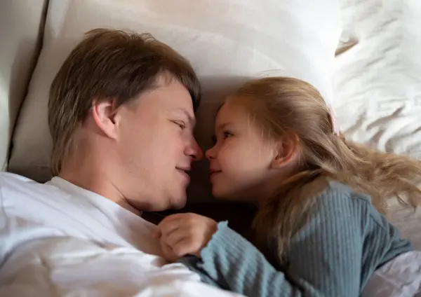 stock image little cute girl hugging her dad while lying in bed.