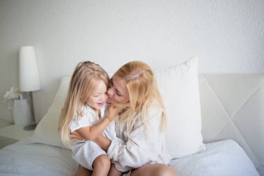 Küçük kız yatak odasında yatakta otururken annesine sarılıyor..