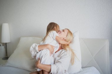 Küçük kız yatak odasında yatakta otururken annesine sarılıyor..