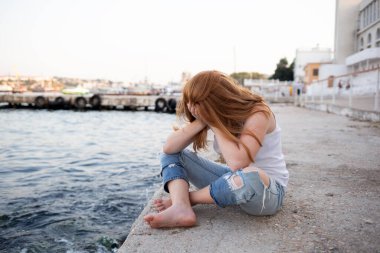 Kızıl saçlı genç bir kız deniz kıyısında oturuyor. Sorunlu gençlik konsepti, depresif durumlar..