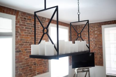 Modern minimalist chandelier with candles against an exposed brick wall in a cozy room. clipart