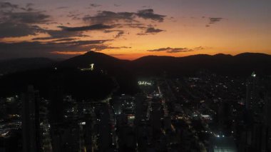 Günbatımında Balnear io Camboriu 'ya tepeden bakan ikonik İsa' nın çarpıcı hava manzarası. Şehir ışıkları parlamaya başlıyor..