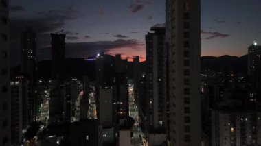 Çarpıcı bir insansız hava aracı, uzak bir yamaçtan görünen İsa heykeli ve yüksek binalar arasında akan trafiğin olduğu bir şehir caddesini akşam karanlığında yakalıyor..