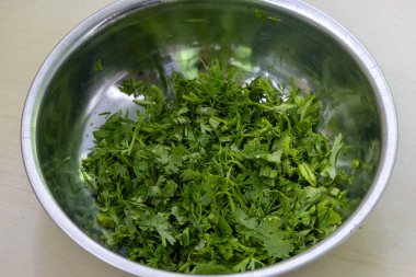 Fresh coriander leaves in a steel bowl on wooden background. Cilantro is another name for the leaves of the coriander plant, Coriandrum sativum. It is called locally Dhone Pata in Bangladesh. clipart