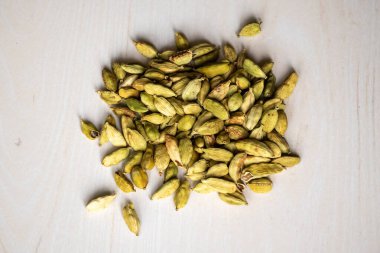 A pile of cardamom pods isolated on a wooden background. locally in Bangladesh, it is called Elachi and Its scientific name is Elettaria cardamomum. Top view. clipart