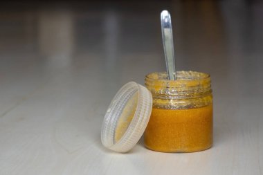 A jar of ghee or clarified butter with a steel spoon on a wooden textured background. Ghee is rich in important nutrients like vitamin A, omega-3 fatty acids, and conjugated linoleic acid. clipart