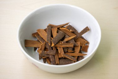 Tahta arka planda beyaz bir kasede tarçın çubukları (Cinnamomum verum) yığını. Darchini, Daruchini ve Dalchini olarak da bilinir..