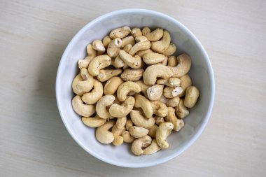 Tahta arka planda beyaz bir kasede sağlıklı kaju fıstığı. Bilimsel adı Anacardium occidentale 'dir ve Bengalce' de buna Kaju Badam denir. Üst görünüm.