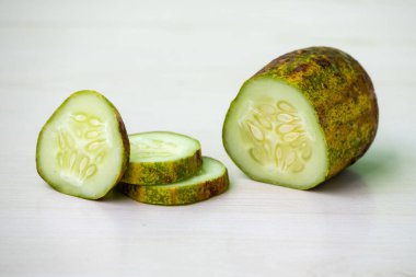Fresh cucumber and cucumber slices on white textured wooden background clipart