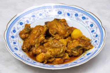 Beyaz arka planda tabakta leziz bir körili tavuk. Bengali 'nin (Bangladeş) tavuk eti, patates ve baharatlı soslu mutfağının yakın çekim görüntüsü. Lezzetli Asya yemekleri.