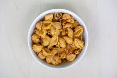 Ahşap arka planda beyaz bir kasede lezzetli kabuklu makarna. Lezzetli conchiglie rigate makarnasının üst görüntüsü.