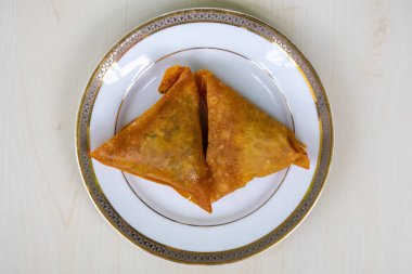 Beyaz tabakta iki samosa. Asya Lezzetli Yemekler Sambusa, singara, samose, somsa, singada ve samuza olarak bilinir. Üst görünüm