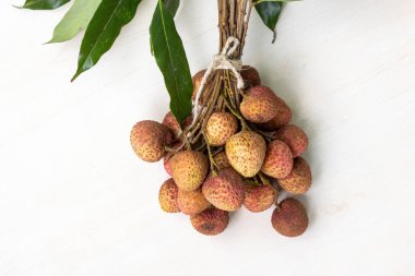 Beyaz ahşap bir yüzeye yerleştirilmiş bir ip ile birbirine bağlanmış bir sürü taze liçi. Lychees 'in kırmızı-kahverengi bir teni var..