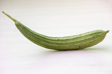 A single angled luffa gourd on a light wooden surface. It is also known as Chinese okra, Silk squash, Ridge gourds, Jhinga, and Turai. clipart