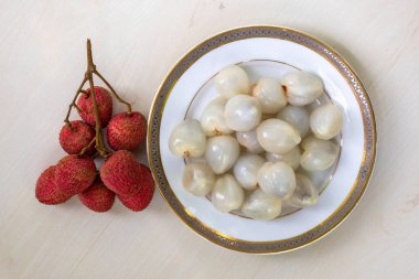 Tahta arka planda beyaz bir tabakta olgun liçi ve soyulmuş litchi. Üst görünüm