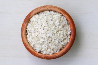 Flattened rice or chira on a earthen pot on a wooden background. It is also known as poha, pohe, aval, pauwa, sira, chivda, or avalakki. clipart