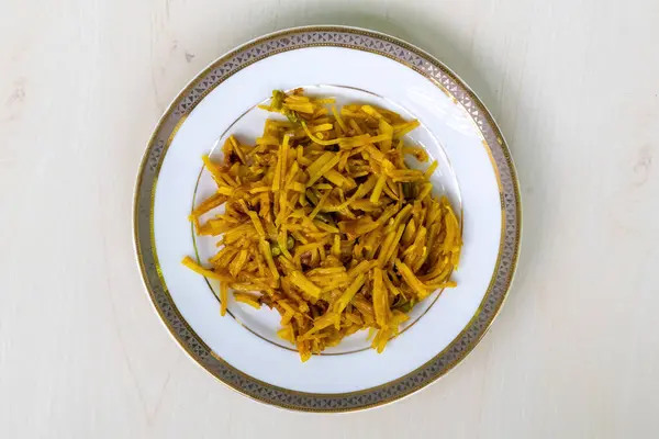 stock image Aloo bhaji or fried grated potato in a white plate on wooden background. Authentic bengali food which is thin potato slices deep fried using turmeric and some mild spices. Top view