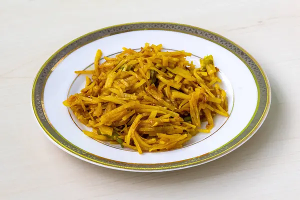 Stock image Delicious aloo bhaji or fried grated potato in a white plate on wooden background. Authentic bengali food which is thin potato slices deep fried using turmeric and some mild spices.