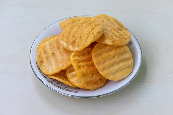 Stock image Crispy delicious potato chips on a white plate on light wooden background. Alooz crackers sour cream and onion flavor.