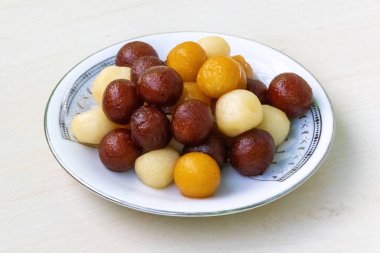 Juicy Bangladeshi sweets on a white plate on light wooden background. It is called Baby sweet because little in size. Very tasty sweet. clipart