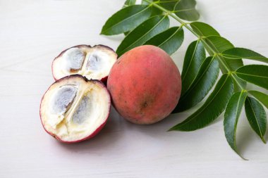 Taze kadife elma (Diospyros blancoi) meyvesi ve ikiye bölünmüş bir meyve, açık ahşap bir yüzey üzerinde sergilenmektedir..