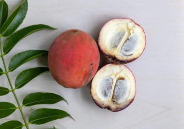 Fresh whole velvet apple (Diospyros blancoi) fruit and one sliced in half, displayed on a light wooden surface. Top view. clipart