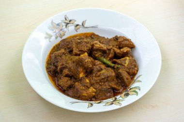 Delicious mutton curry in a white ceramic plate on a wooden background. Mutton bhuna is a popular, flavorful, and spicy Bangladeshi dish. clipart